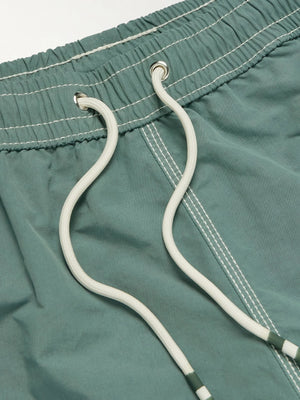 A pair of HARTFORD nylon swim trunks in Faded Kelly with white stitching and side pockets, shown flat on a light background. Includes travel pouch.