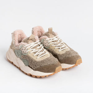 The FLOWER MOUNTAIN - KOTETSU SNEAKER by FLOWER MOUNTAIN/FALC USA is a stylish pair of beige and olive green shearling sneakers, featuring a textured, fluffy lining and trekking-style lacing in white. They come with a thick, white and brown patterned sole and an embroidered flower design on the side. Additionally, they have a pull tab on the heel. The sneakers are displayed against a plain white background.