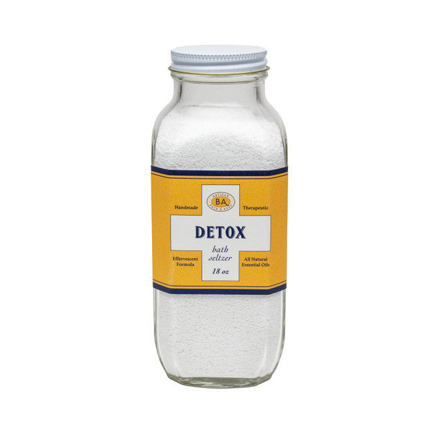 A clear glass jar with a white lid contains white bath salts. The jar&#39;s yellow and blue label reads: &quot;BAUDELAIRE - DETOX BATH SELTZER 18 OZ.&quot; Additional text indicates it is handmade, therapeutic, all-natural with essential oils and natural ingredients, featuring a proprietary formula.