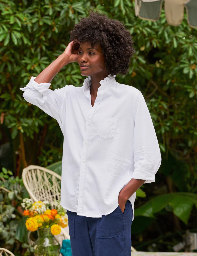 The FRANK &amp; EILEEN Ruffle Eileen Ruffle Collar Button Up Shirt in White Famous Denim features rolled-up long sleeves, a ruffled collar, and a single chest pocket, shown against a white background.