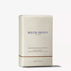 A rectangular beige MOLTON BROWN RE-CHARGE BLACK PEPPER BODY SCRUB BAR (250g) with small dark specks and "MOLTON BROWN LONDON" in gold across the front.