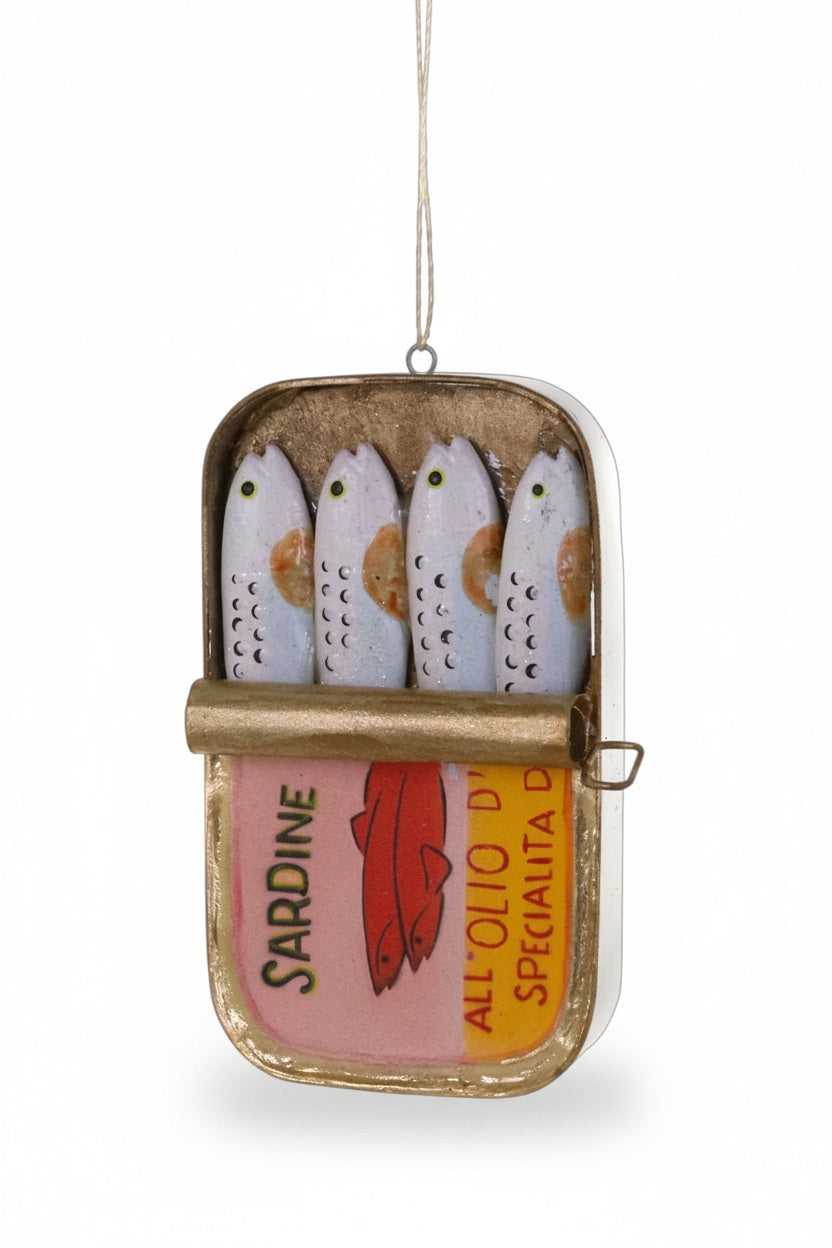 A Cody Foster PACKAGED SARDINES ORNAMENT shaped like an open resin tin containing four fish, with a label printed with “SARDINE” and “ALL ‘OLIO D’”.