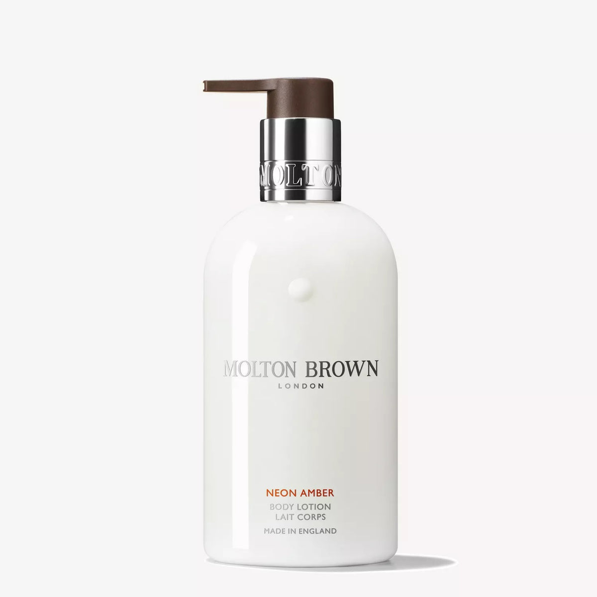 A white 300ml bottle of MOLTON BROWN Neon Amber Body Lotion, infused with amber and tonka absolute, features a silver collar and brown pump dispenser against a plain light background.