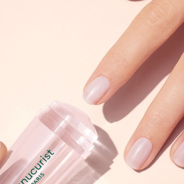 A hand with a light pink French manicure rests beside the MANUCURIST - MANI STAMPER by MANUCURIST INC on a pale background.