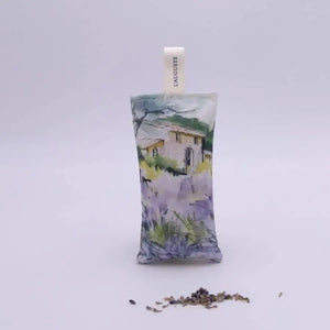 The L'AUGUSTE PROVENCE - FRENCH LAVENDER SACHET FROM PROVENCE features a painted house in a lavender field, stands upright with dried lavender in front, and is topped with a white "L'AUGUSTE" ribbon—authentic from Provence.