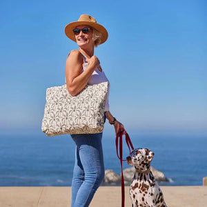 The ROCKFLOWERPAPER PALM SHOPPER TOTE BAG is a spacious cotton canvas bag with two handles, featuring a stylish brown palm tree print on a white background.