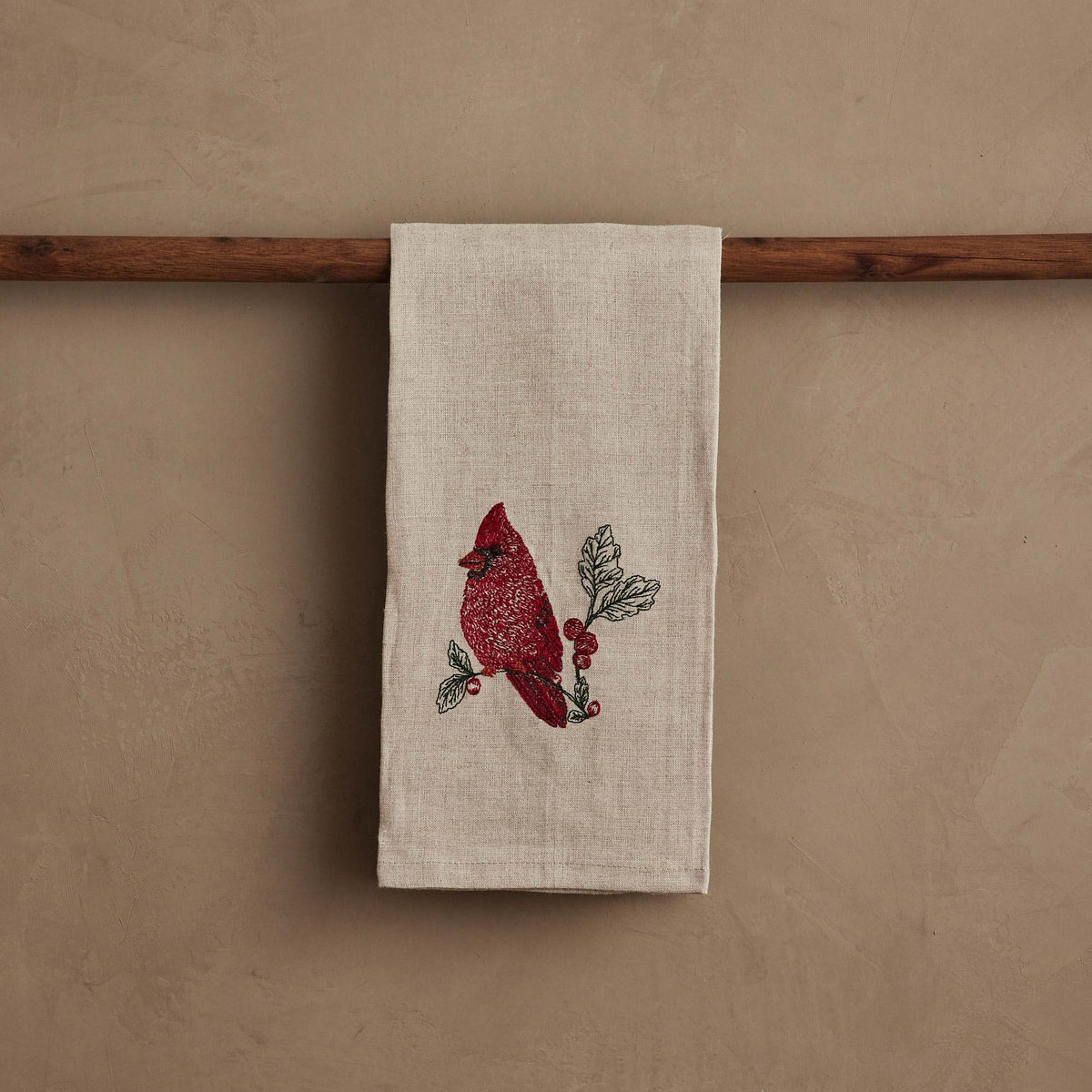 A RED CARDINAL LINEN TEA TOWEL by CORAL & TUSK made of beige natural flax fiber, embroidered with a red cardinal perched on a branch with berries and green leaves.