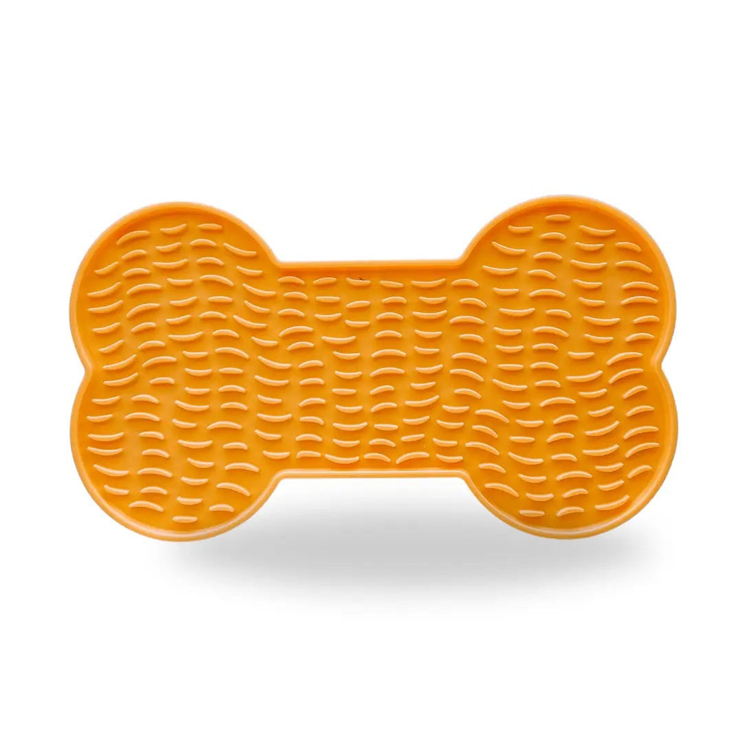 The BONE LICK MAT - ORANGE by BARKS & BROWNIES is an orange, bone-shaped silicone slow feeder mat featuring raised ridges, designed to encourage pets to lick food or treats from its textured surface and promote anxiety relief during mealtime.