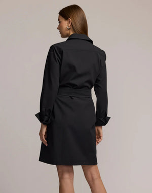 A woman with straight brown hair wears the HINSON WU Astrid Long Sleeve Traveler’s Twill Dress in black, featuring a collared neckline and tie waist, standing with her back to the camera against a neutral background.
