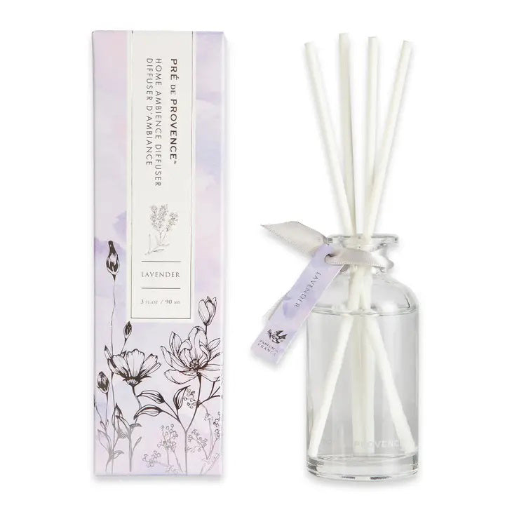 A clear glass bottle from the HERITAGE REED DIFFUSER - LAVENDER set by EUROPEAN SOAPS, LLC is displayed. The bottle contains a liquid fragrance with several white diffuser reeds inserted. Made in France, the packaging features a floral illustration and soft pastel colors, underscoring its commitment to quality products.