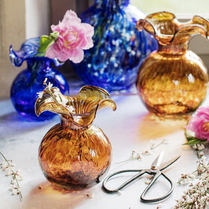 The VIETRI Hibiscus Bud Vase in Tortoiseshell is a round, brown glass vase with a wide, flared wavy rim and a spotted pattern, resembling tortoiseshell, displayed against a white background.