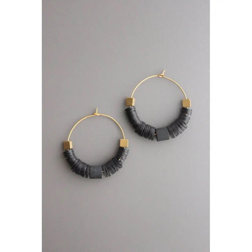 DAVID AUBREY - BLACK VULCANITE HOOP EARRINGS feature thin 18k gold plated wire hoops accented with stacked black discs and gold hexagonal beads, showcased against a plain gray background.