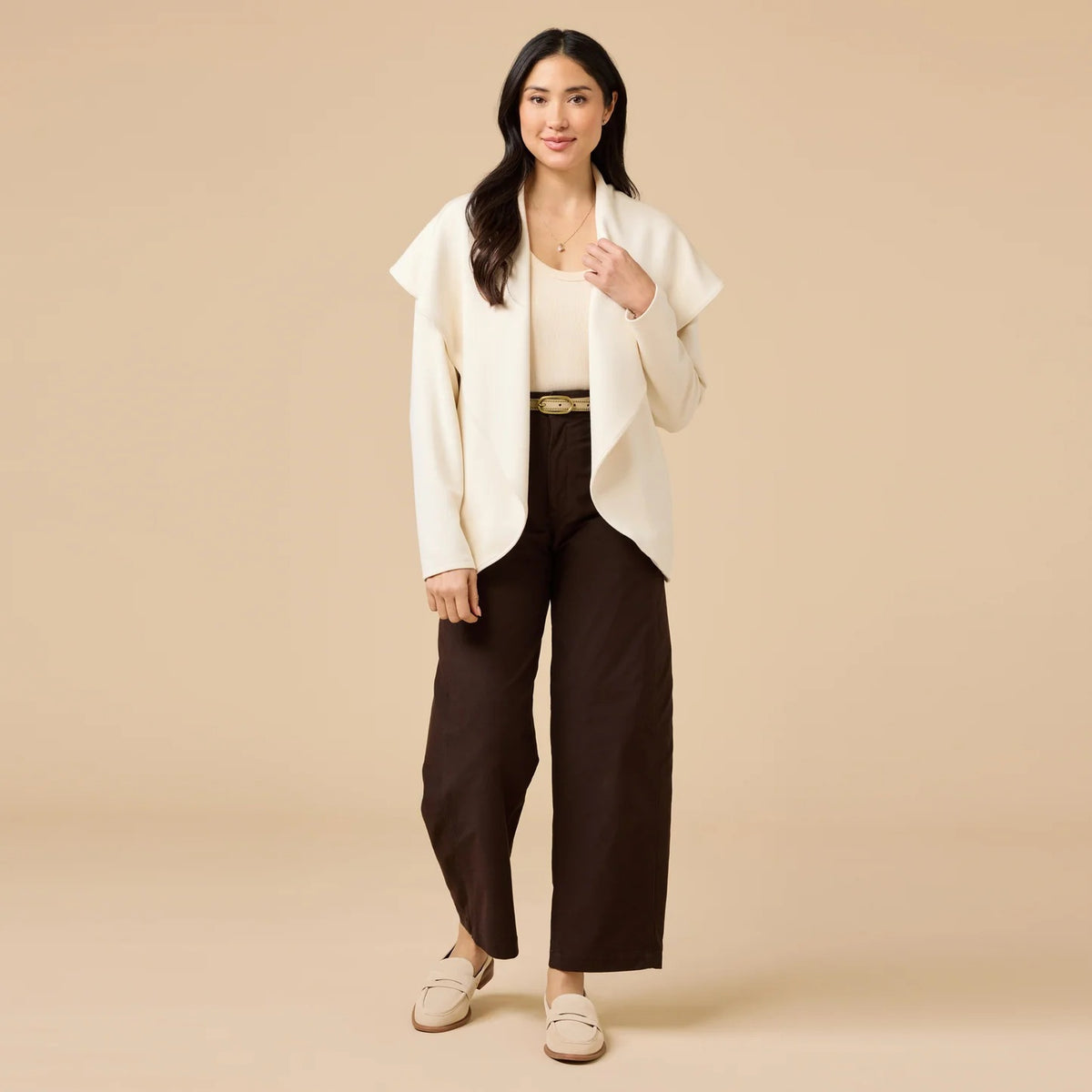 A woman wears an off-white SOFTIES - DREAMTECH EXAGGERATED COLLAR CARDIGAN with an exaggerated waterfall collar, cinched at the waist with a thin belt, and holds a matching handbag.