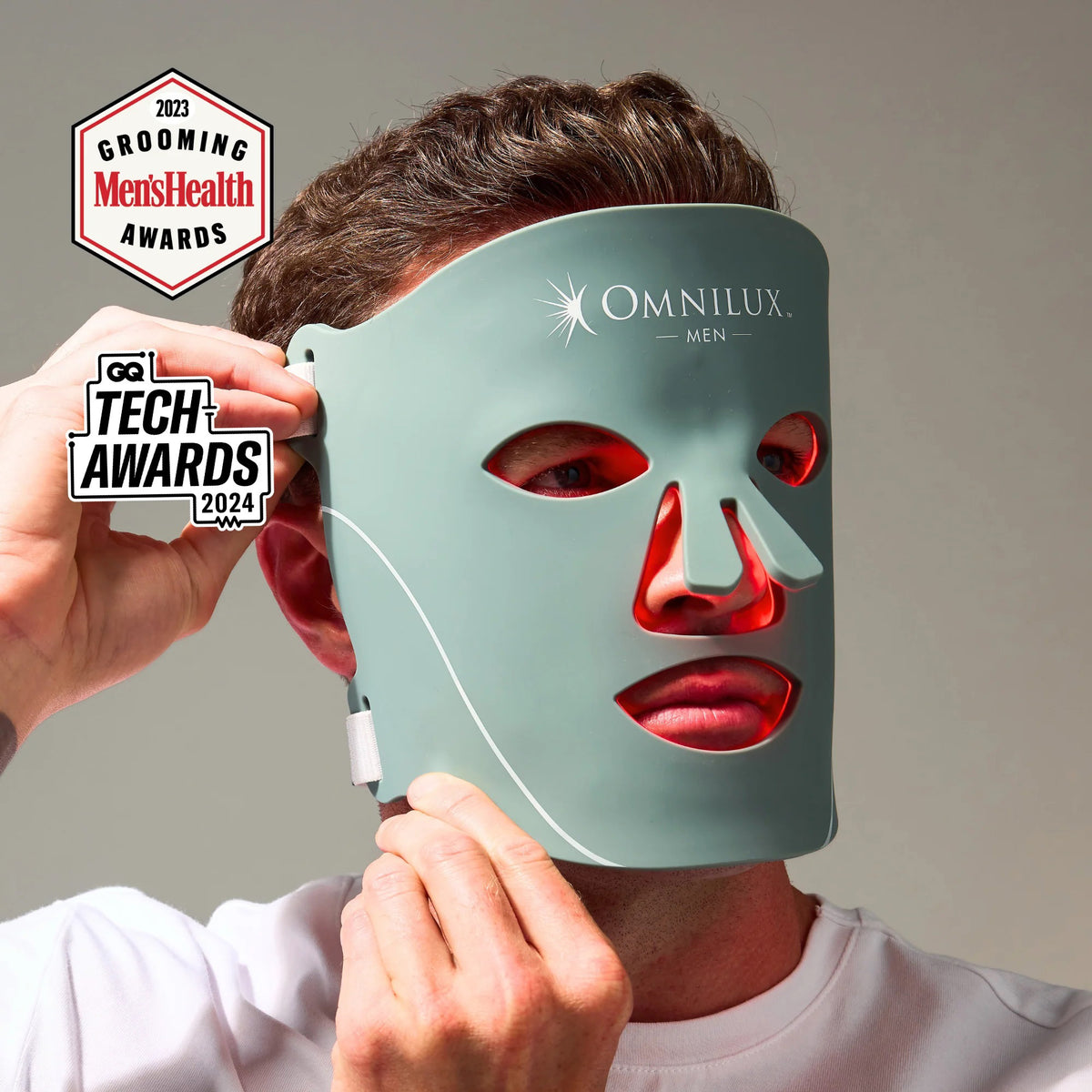 A man intently examines the OMNILUX - MENS MASK, a glowing red LED mask designed for skin rejuvenation with advanced red light therapy, featuring eye, nose, and mouth cutouts.