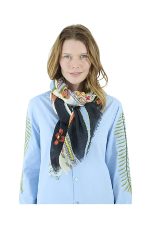 The STORIATIPIC ARIANE wool scarf with embroidery is adorned with a floral and vine pattern in red, green, blue, cream, and black tones. It features light blue edges and a soft, slightly fringed border. The embroidered scarf is loosely knotted against a white background.