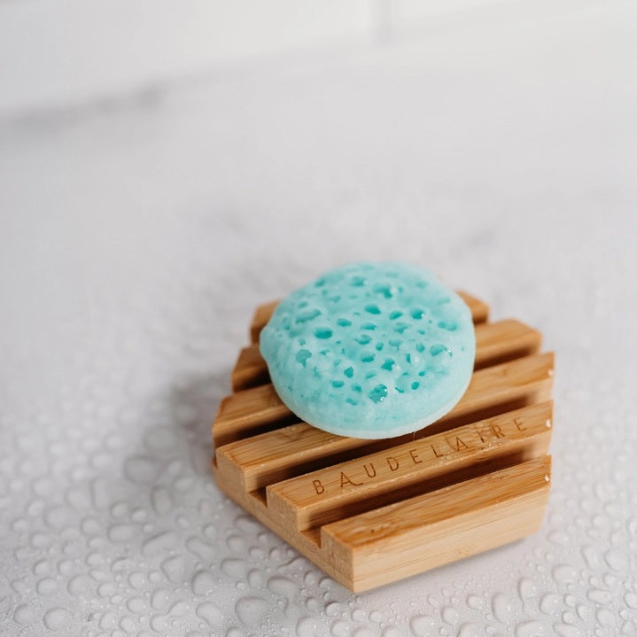 A white box labeled “BAUDELAIRE - REPLENISH EUCALYPTUS RAIN SHOWER STEAMER” by BAUDELAIRE, featuring a window that displays stacked round blue and white shower steamers inside, provides a refreshing aromatherapy experience with the invigorating scent of eucalyptus.