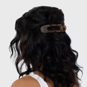 Two sustainable rectangular hair clips, one solid black and the other with a brown and black tortoiseshell pattern, rest on a light pink card. The card emphasizes the recycled materials of "KITSCH - FLAT LAY CLAW CLIP 2 PC," showcasing their style and eco-friendly commitment.
