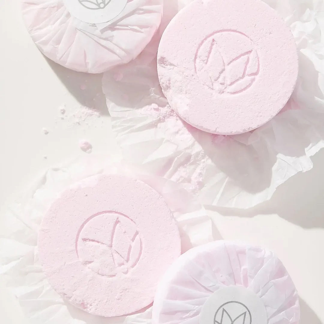 Four round white shower steamers are placed in front of a pink MUSEE package labeled “MUSEE - CHAMPAGNE & ROSE SHOWER STEAMERS” in gold and white text with a small showerhead graphic above, offering a natural bath product designed to turn your daily routine into a luxurious spa shower experience.