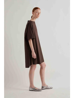 A person with straight red hair stands against a plain light background, wearing the MEIMEIJ oversized cotton shift dress in black by MEIMEIJ and silver flat shoes.