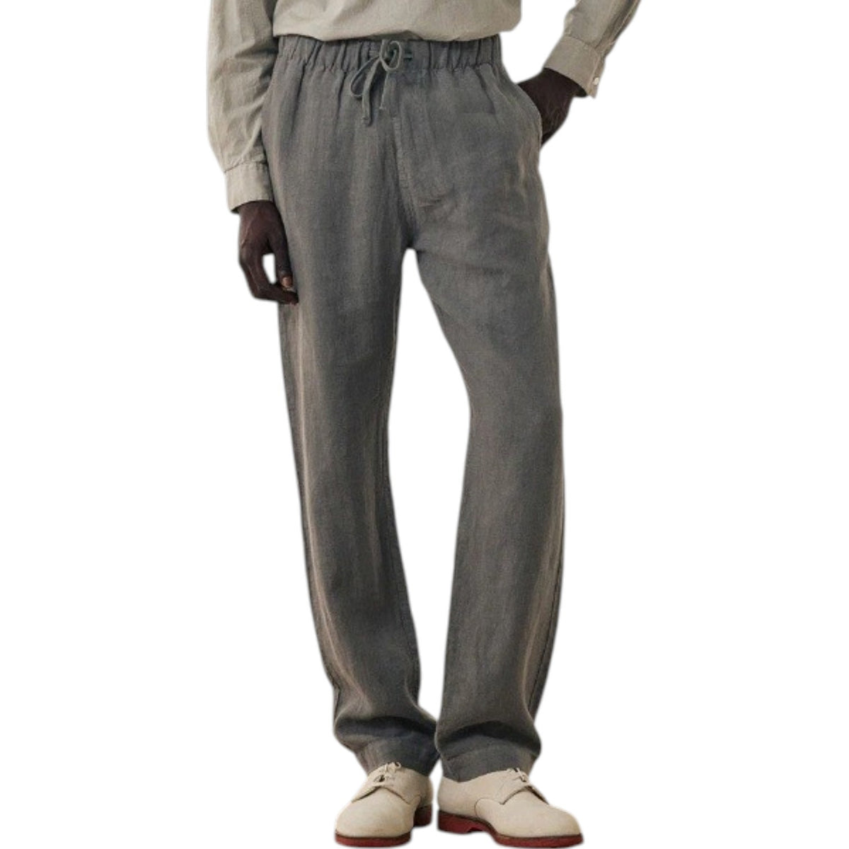 A man stands against a plain background wearing a light gray long-sleeve henley shirt, HARTFORD - LINEN JOGGY PANTS IN ARMY, and light-colored shoes, with his hands in his pockets.