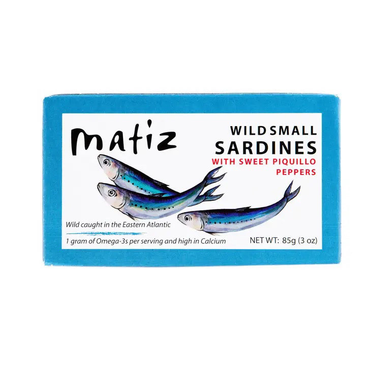 A rectangular package of MATIZ ESPANA Matiz - Sardinillas with Piquillo Peppers in Spanish Olive Oil. The blue package showcases an illustration of three sardines and includes details such as "Wild caught in the Eastern Atlantic," "1 gram of Omega-3's per serving," and "NET WT: 85g (3 oz).