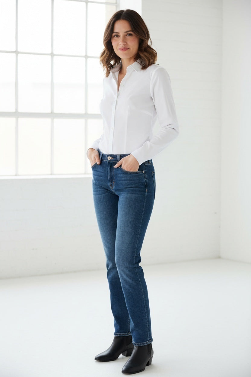 A woman with shoulder-length dark hair stands facing forward against a plain light background, wearing the HINSON WU Jamie Long Sleeve “T” Shirt in White crafted from stretch polished cotton and blue jeans, showcasing the refined finish of this versatile look.