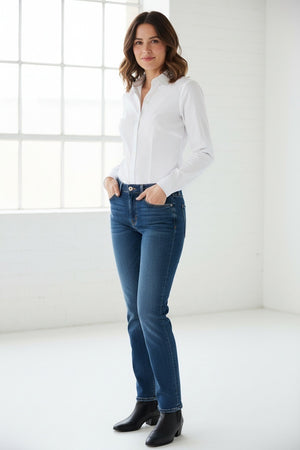 A woman with shoulder-length dark hair stands facing forward against a plain light background, wearing the HINSON WU Jamie Long Sleeve “T” Shirt in White crafted from stretch polished cotton and blue jeans, showcasing the refined finish of this versatile look.