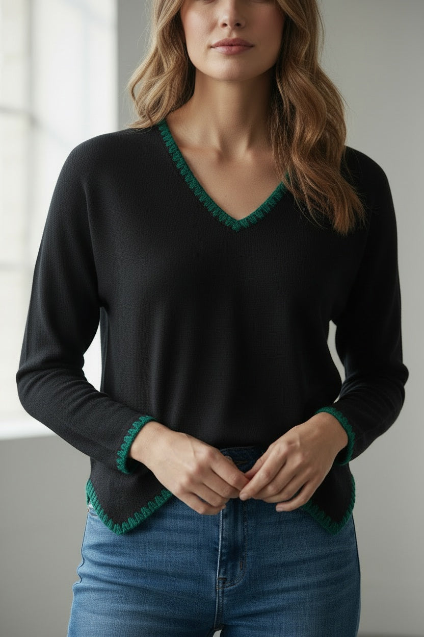 A person with light blonde hair stands sideways against a white background, wearing the MEIMEIJ V Neck Hi Low Top with embroidered contrast stitch detail by MEIMEIJ, paired with white pants.