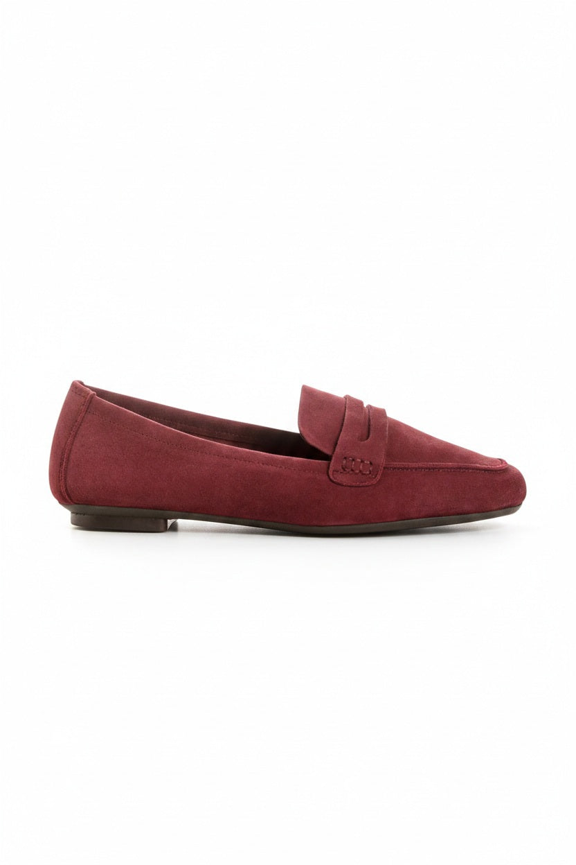 Close-up of the REQINS - HEMA SUEDE LOAFER IN BORDEAUX by REQINS, showcasing artisanal craftsmanship with burgundy suede, detailed stitching, a front strap, and a soft leather insole, displayed on a light surface.