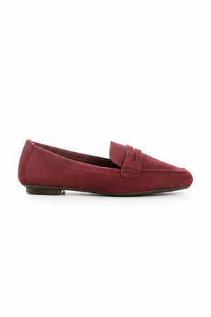 Close-up of the REQINS - HEMA SUEDE LOAFER IN BORDEAUX by REQINS, showcasing artisanal craftsmanship with burgundy suede, detailed stitching, a front strap, and a soft leather insole, displayed on a light surface.