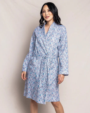 The PETITE PLUME - FLEUR D'AZURE ROBE by PETITE PLUME is a knee-length, long-sleeved bathrobe adorned with a vintage-inspired floral print in blue and white hues. Crafted from the finest quality cotton, the robe features a shawl collar and includes a matching fabric belt tied at the waist. It offers a relaxed fit ideal for comfortable lounging in luxurious sleepwear.