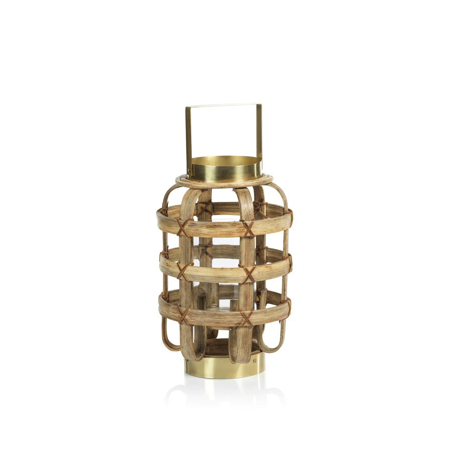 The ZODAX Bamboo Lantern with Brass Trim is a decorative lantern featuring a rustic design. It has a woven, cage-like structure made of bamboo slats held together with red twine. The lantern boasts a brass base, top, and handle, creating a harmonious blend of natural and metallic aesthetics. Dimensions: 20.32 cm x 20.32 cm x 33.02 cm (8 in x 8 in x 13 in).