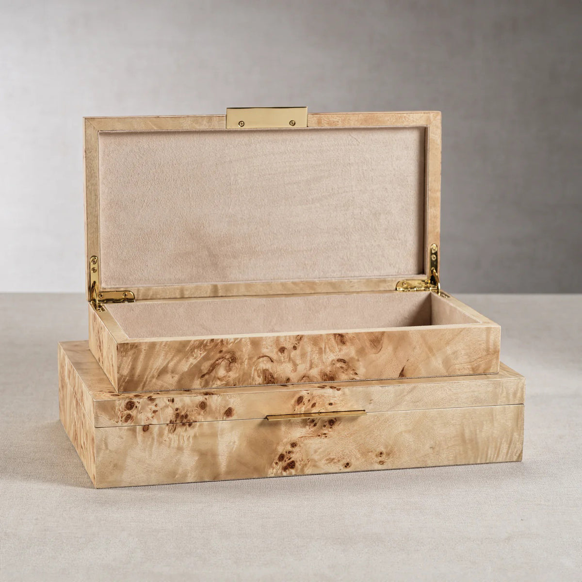 The ZODAX BURL WOOD VENEER BOX - SMALL features a hinged lid and smooth, light interior. Its natural wood grain finish stands out on a gray surface against a neutral background.