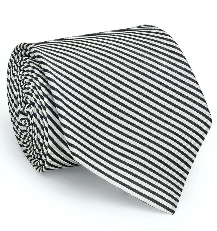 A rolled-up COLLARED GREENS - SIGNATURE STRIPE TIE IN BLACK by BIRD DOG BAY, handmade in New York from luxurious woven silk, featuring black and white diagonal stripes displayed against a white background.