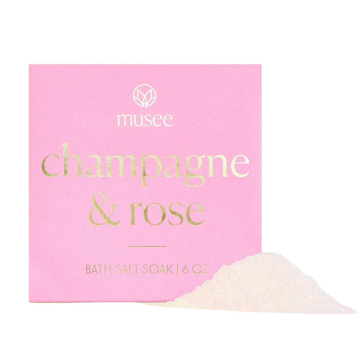 A pink box labeled “MUSEE - CHAMPAGNE & ROSE MINI BATH SALT SOAK” in gold lettering, with a small pile of white bath salt crystals displayed in front.