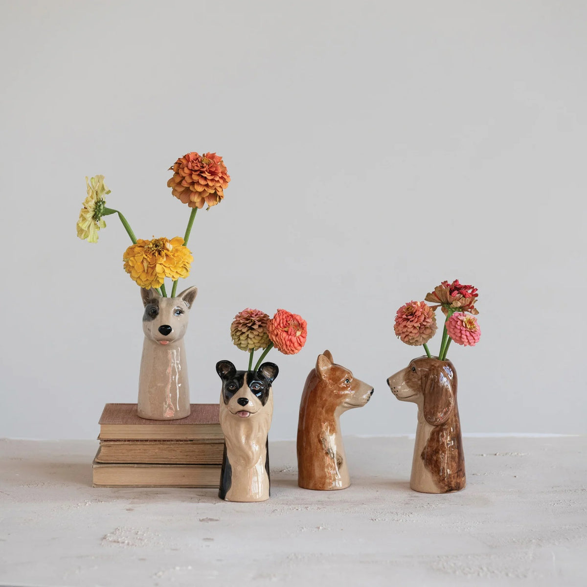 Four small, glossy CERAMIC animal vases, including the hand-painted STONEWARE DOG VASE by CREATIVE COOP in brown and a black pet-themed décor piece with round ears, all shown from the back.