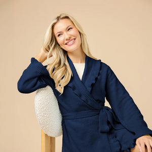A woman wearing a SOFTIES - RUFFLE CHENILLE ROBE 36″ IN MIDNIGHT, a knee-length navy blue chenille robe with cascading ruffle trim.