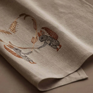 SQUIRRELS WITH WHEAT HEART LINEN TEA TOWEL by CORAL & TUSK featuring two embroidered squirrels holding stalks of wheat that form a heart shape above them.