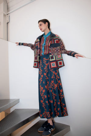 The FRANCO FERRARI JEMMA Wool Midi Skirt is a long, dark blue A-line skirt with red and orange floral prints and green stems, shown on a plain white background.