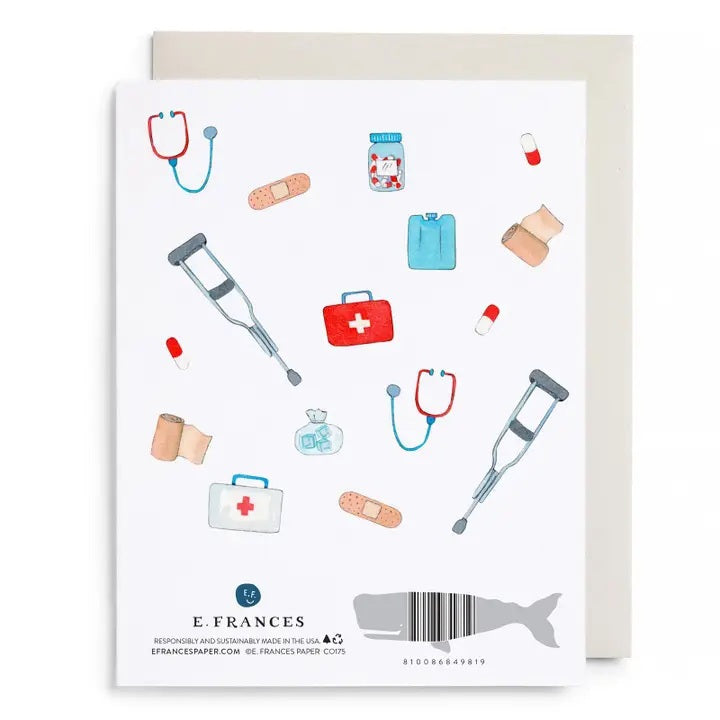 The E. FRANCES - FIRST AID KIT CARD from E. FRANCES PAPER is a watercolor greeting card featuring "Get Well Soon" in gold letters, surrounded by illustrations of crutches, stethoscopes, bandages, pills, first aid kits, pill bottles, and an ice pack on a white background—thoughtfully designed as a sympathy card and proudly made in the USA.