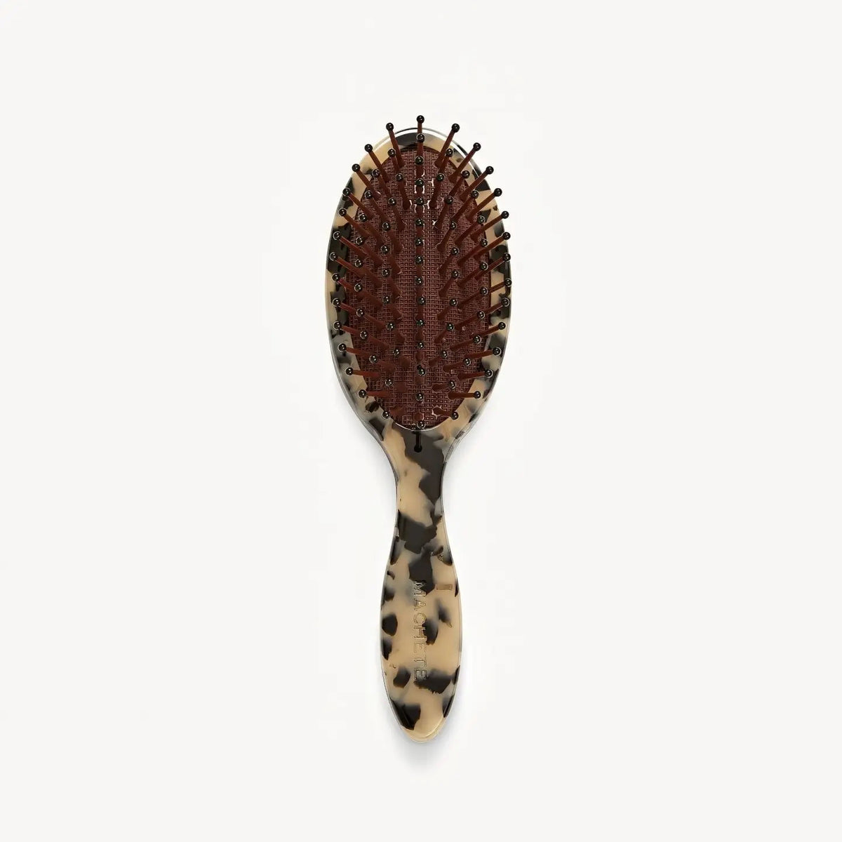The MACHETE Petite Travel Detangling Hair Brush in Blonde Tortoise features nylon bristles on a brown cushioned pad and a marbled beige-and-black Italian acetate handle—ideal as a compact travel brush.