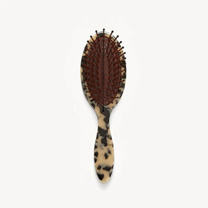 The MACHETE Petite Travel Detangling Hair Brush in Blonde Tortoise features nylon bristles on a brown cushioned pad and a marbled beige-and-black Italian acetate handle—ideal as a compact travel brush.