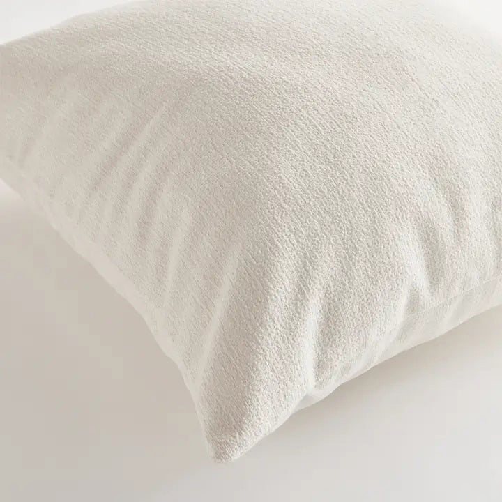 The NAPA HOME AND GARDEN - COOPER SQUARE OUTDOOR PILLOW 24&quot; is a plain, light beige cushion with soft, textured recycled fabric. Plush and comfortable, it&#39;s ideal for sofas or beds. Shown against a white background.