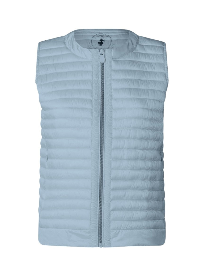 An older woman with short gray hair wears the SAVE THE DUCK - MARA PUFFER VEST over a white t-shirt and beige pants, standing against a light background—perfect for spring–summer layering from SAVE THE DUCK.