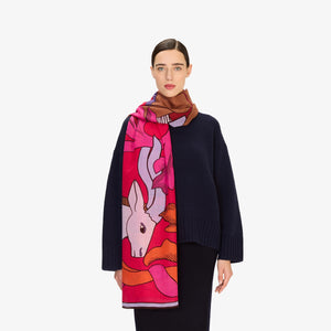 Close-up of the INOUI EDITIONS - CAVALE WOOL SCARF IN RED by INOUI, featuring crumpled wool in red, pink, and orange with dark brown abstract lines. Its woven texture and bold style make it a perfect winter accessory.