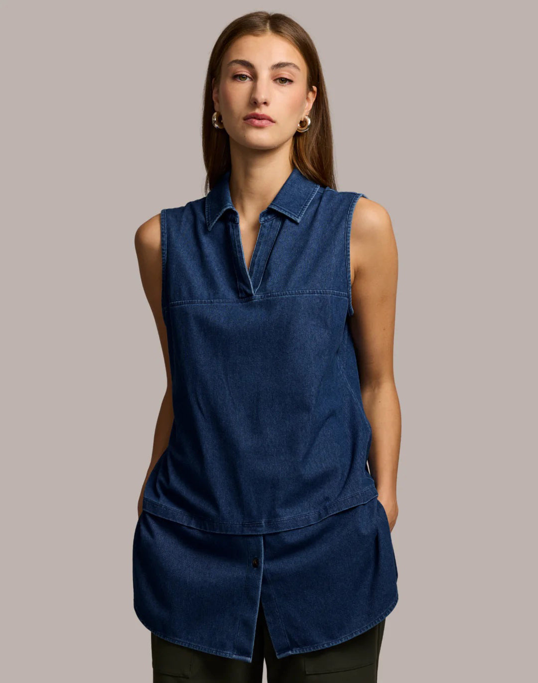 A woman with straight brown hair wears the HINSON WU LEA Sleeveless Foundation Layer in Denim Dark Wash, standing with hands in pockets against a light beige background.