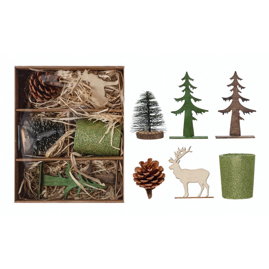 The CREATIVE COOP GARDEN KIT WITH HOLIDAY TREE features pine cones, green glittery candle holders, a bottle brush tree, and wooden cutouts of fir trees and a reindeer, all beautifully arranged on straw.