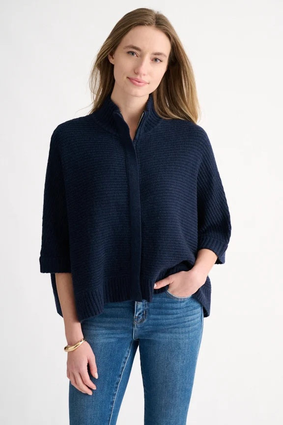 A person wears the KINROSS Rib Zip Mock Sleeveless Cardigan in Navy by KINROSS, paired with blue jeans. They stand against a plain white background, smiling slightly with one hand in their pocket.