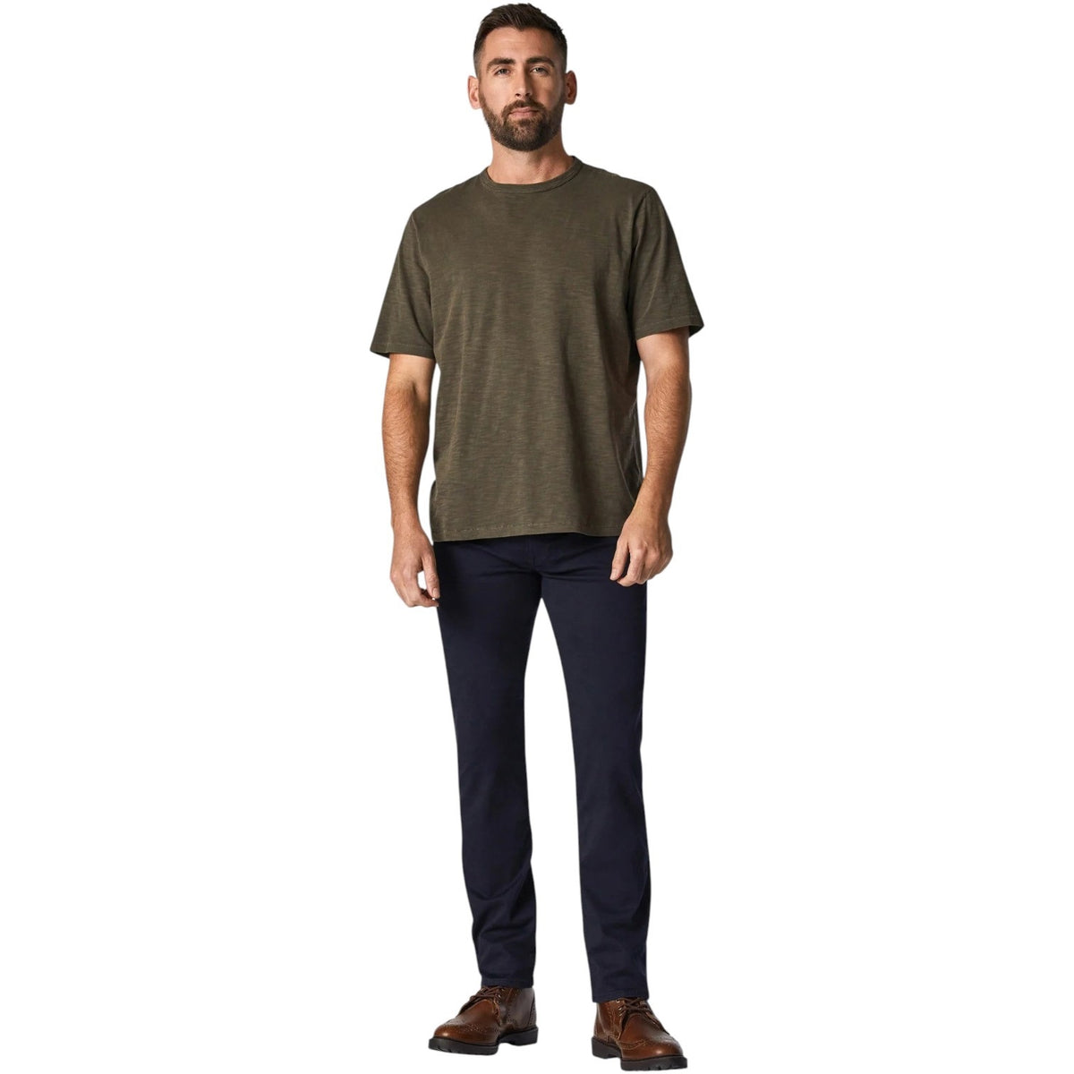 A man with short hair and a beard stands facing forward, wearing an olive green T-shirt, 34 HERITAGE - COURAGE STRAIGHT LEG PANT IN NAVY TWILL, and brown shoes against a plain white background.