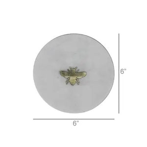 The HOMART MARBLE TRAY INLAID WITH BRASS BEE is a round, white marble tray featuring a small brass bee at the center and measures 6 inches in diameter.